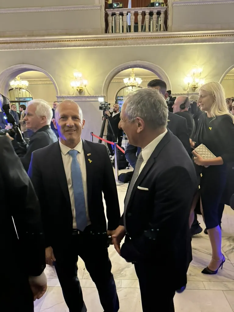 השגריר ראובן עזר ועו״ד אילן ליבוביץ משוחחים באולם האופרה, צלמי טלוויזיה ברקע